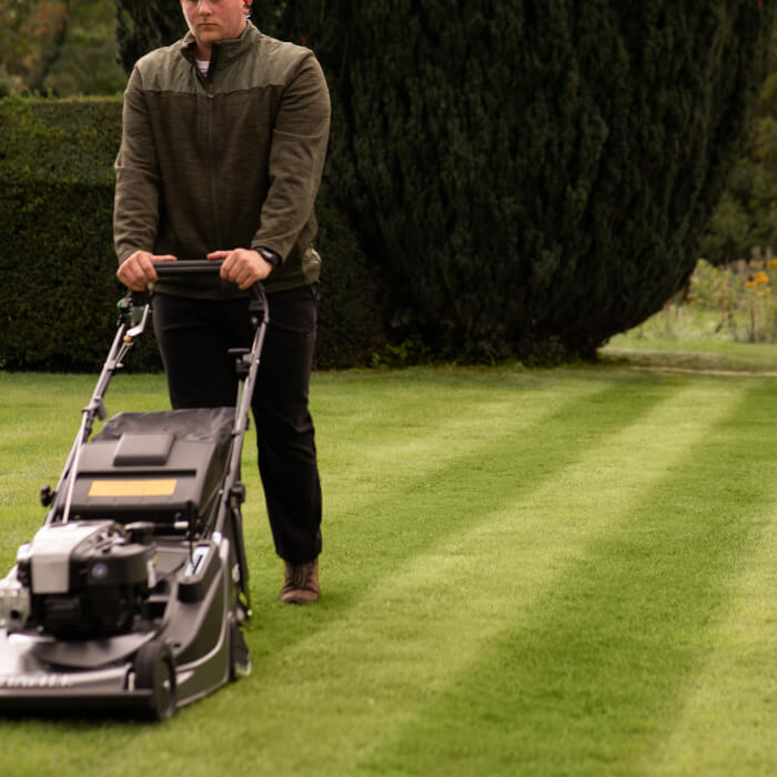 A professional landscaper mowing with the Hayter Harrier 56 Pro, creating immaculate striped patterns on a well-maintained lawn. The mower’s rear roller ensures a flawless finish, ideal for high-end gardens and professional grounds maintenance.