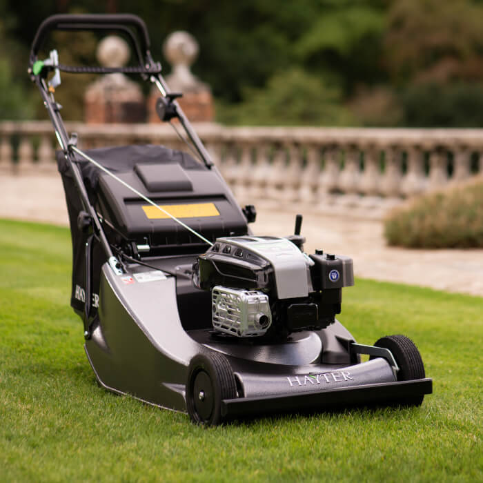 A close-up view of the Hayter Harrier 56 Pro lawnmower, highlighting its durable build, powerful engine, and professional-grade finish. The mower sits on a lush green lawn, ready for high-performance cutting.